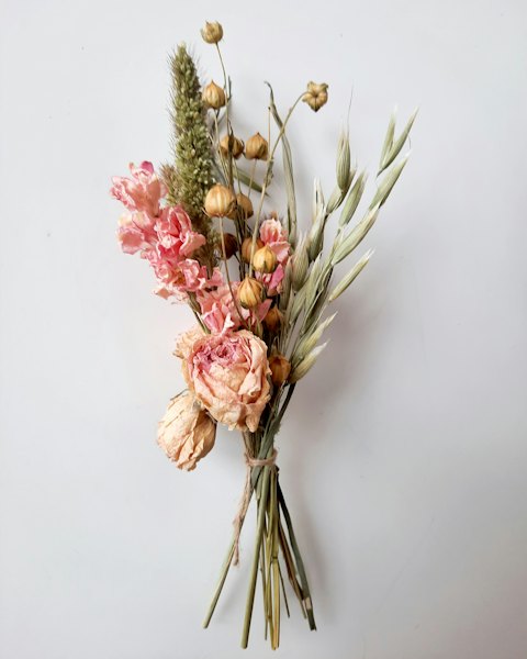 A hand-tied posy of dried roses, poppy seed heads and oat grass