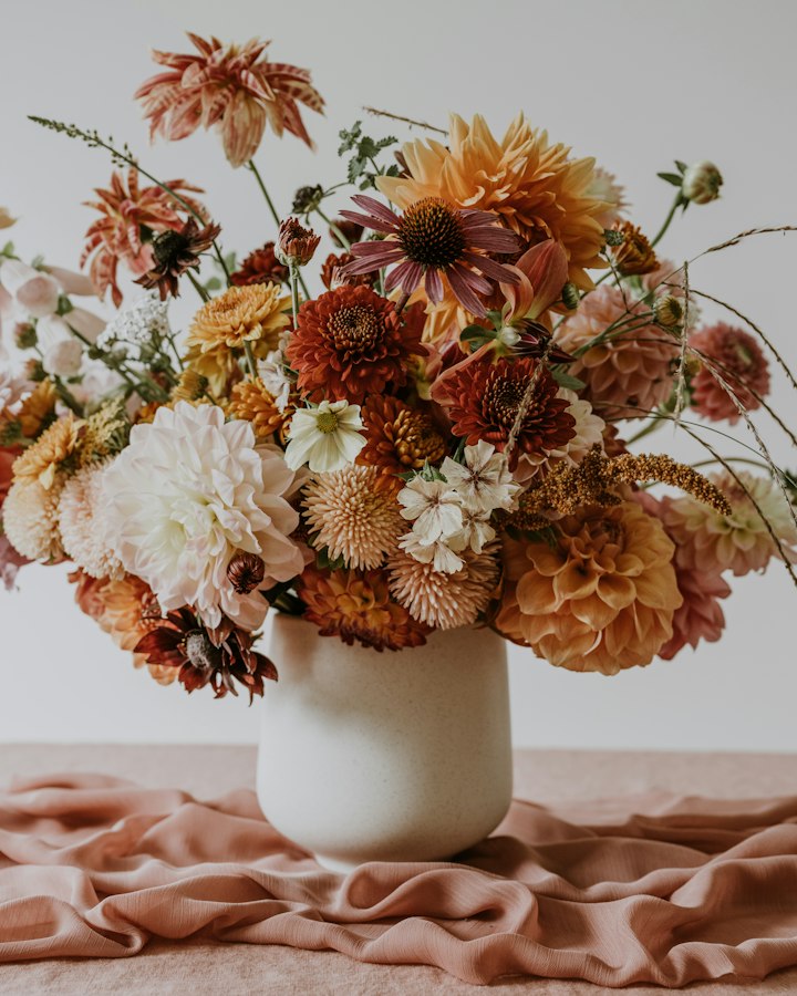 Late Garden arrangement of dahlias, scabiosa and grasses in a cream stoneware vase on blush linen