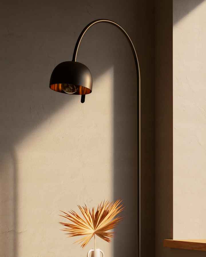 Kasa arc floor lamp with a black dome shade and brass interior, against a sunlit plaster wall
