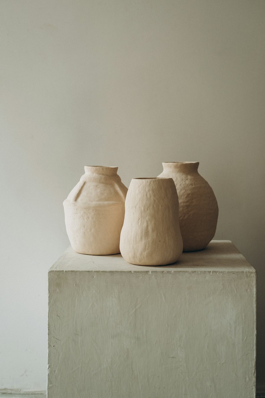 Three hand-built stoneware vases in raw sand clay on a plaster plinth