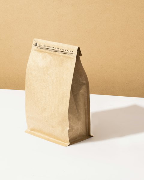 An unbranded kraft paper coffee bag with a resealable top, standing on a white table.