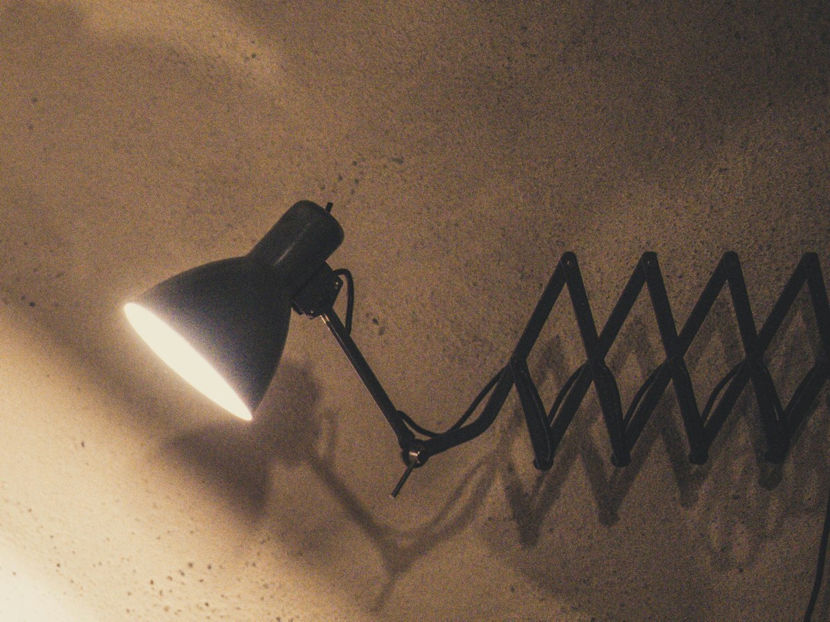 A black scissor-arm lamp glowing against the bare plaster wall of the roastery