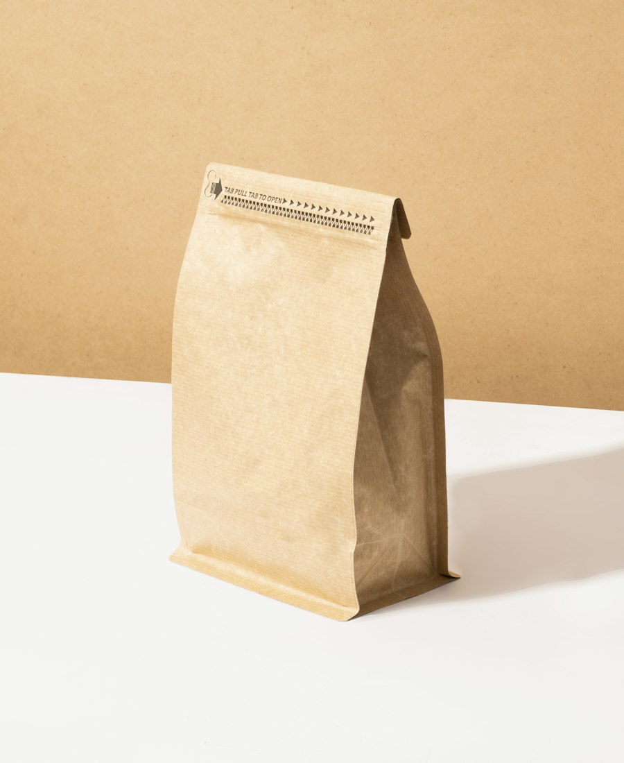A kraft coffee bag with a resealable top standing on a white table against a warm tan wall