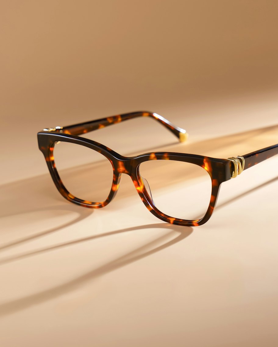 Tortoiseshell cat-eye acetate frames on a warm sand backdrop, casting long shadows