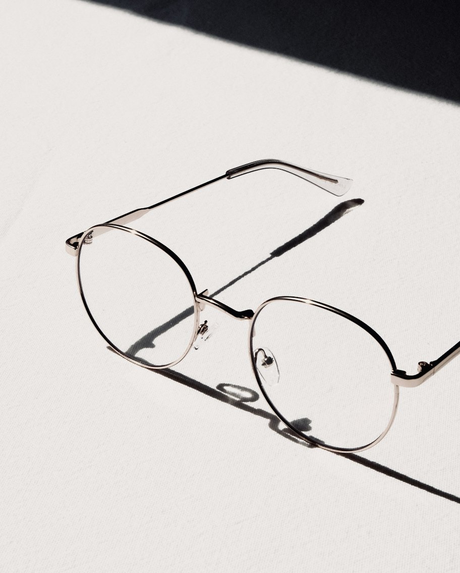 Thin round silver titanium frames on white linen in hard afternoon light