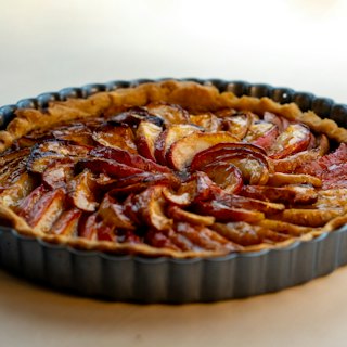 A whole apple tart with fanned, caramelised slices in a fluted tin.
