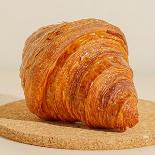 A glossy, deeply laminated butter croissant on a cork board.