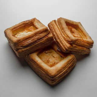 Three square, caramelised kouign-amann pastries stacked on a pale surface.